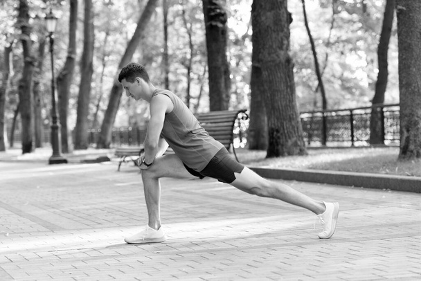 Sportowiec trzymać pozycję longe robi rutynowe rozciąganie podczas treningu sportowego na świeżym powietrzu w parku, rozgrzewka. - Zdjęcie, obraz