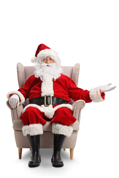 Санта-Клаус сидит в кресле и показывает что-то с рукой изолированы на белом фоне - Фото, изображение