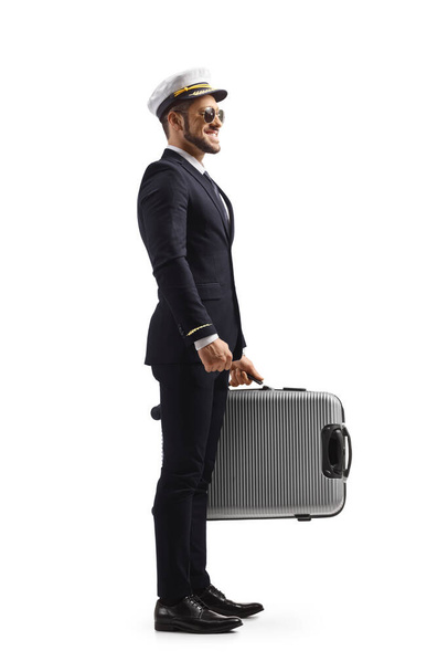 Full length profile shot of a pilot in a uniform standing with a suitcase in his hands isolated on white background - Foto, immagini