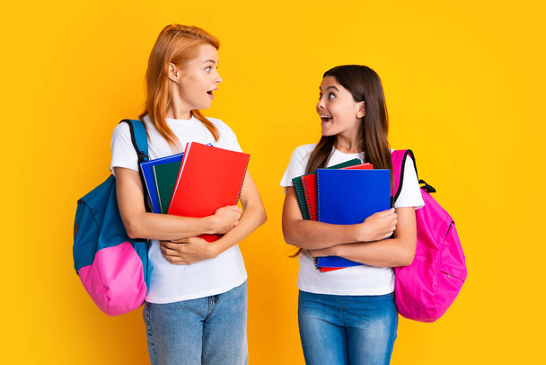 School, learning and education concept. Mother and daughter schoolgirls with school backpack and books ready to learn. Back to school. Mom and child on isolated yellow studio background - Foto, imagen