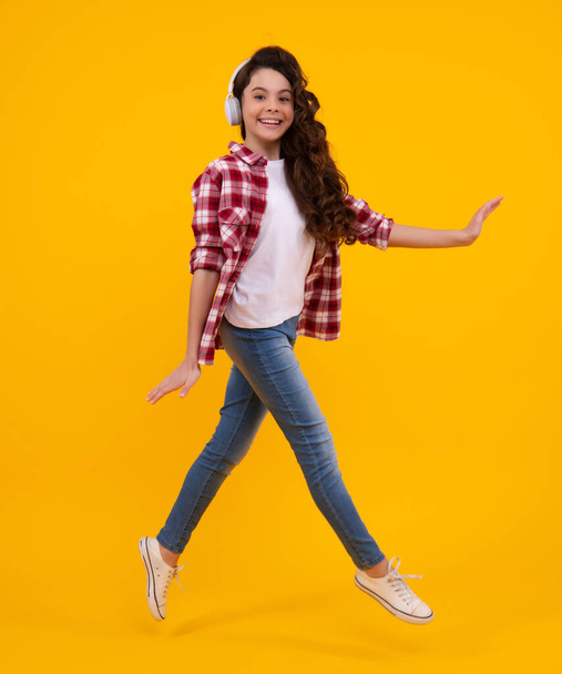Teen girl in headphones listen to music. Wireless headset device accessory. Child enjoys the music in earphones on yellow background. Happy casual teenager. Urban kids style, stylish hipster teen - Fotografie, Obrázek