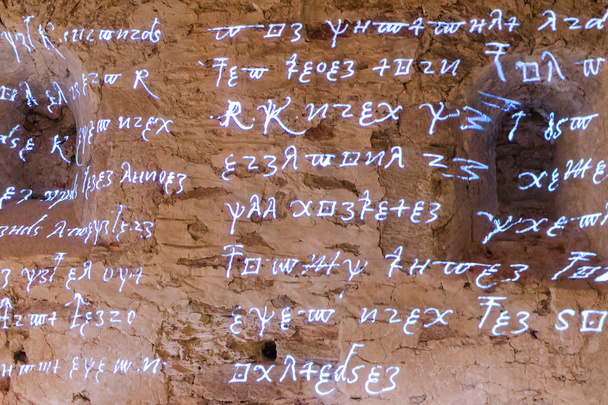 Des runes antiques rougeoyantes caractères et lettres de mots tirés de textes ardents d'écrits anciens sur un mur de pierre brute
 - Photo, image