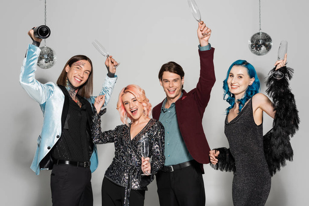 excited and trendy queer people holding champagne glasses in raised hands on grey background - Photo, image