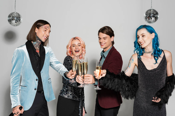 happy and stylish queer friends clinking champagne glasses during new year party on grey background - Zdjęcie, obraz