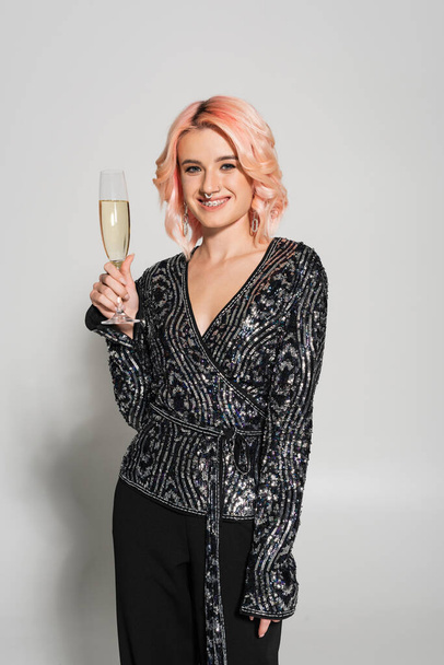 elegant woman in dental braces smiling at camera and holding champagne glass on grey background - Fotoğraf, Görsel