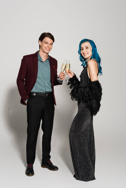 elegant couple smiling at camera and clinking champagne glasses during christmas party on grey background - Φωτογραφία, εικόνα