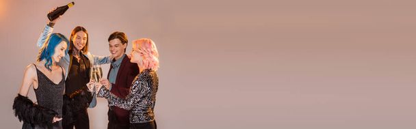 tatuado queer pessoa segurando garrafa de champanhe perto de amigos não binários clinking óculos no fundo cinza, banner - Foto, Imagem