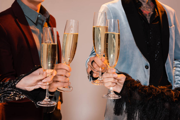 cropped view of people in elegant clothes holding champagne glasses on grey background - Foto, imagen