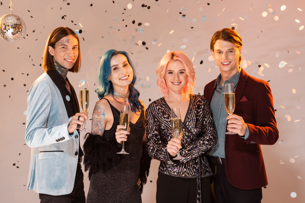 joyful nonbinary people with champagne glasses looking at camera while celebrating christmas on beige background - Photo, Image