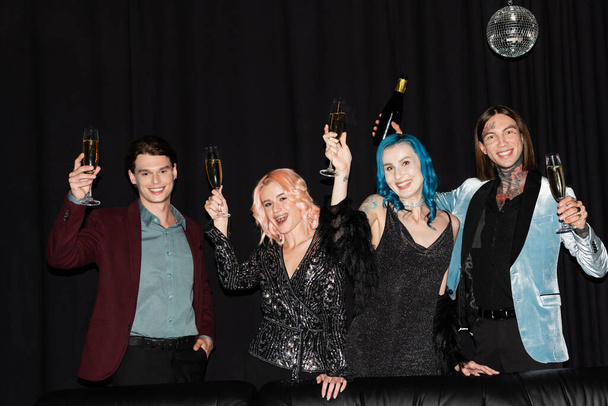persone queer felici ed eleganti brindare con champagne mentre celebrano il Natale e guardando la fotocamera su sfondo nero - Foto, immagini