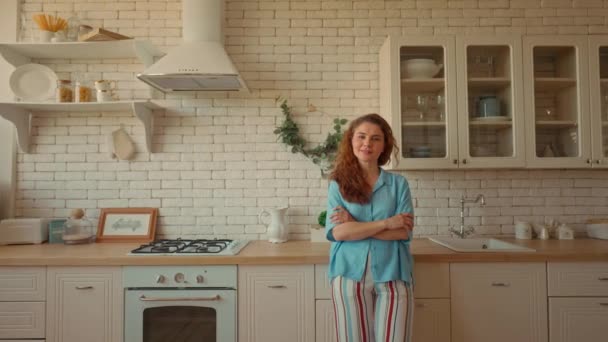 hölgy gyönyörű göndör haj néz kamera boldog tulajdonos lakásban elégedett és elégedett nő pózol a konyhában  - Felvétel, videó