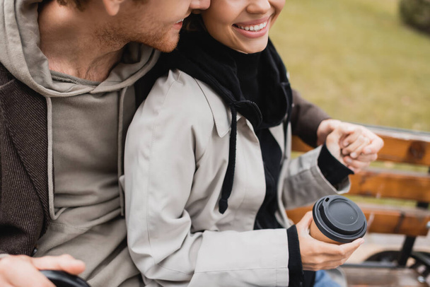 cropped view of happy young man hugging girlfriend holding paper cup with coffee to go - Foto, immagini