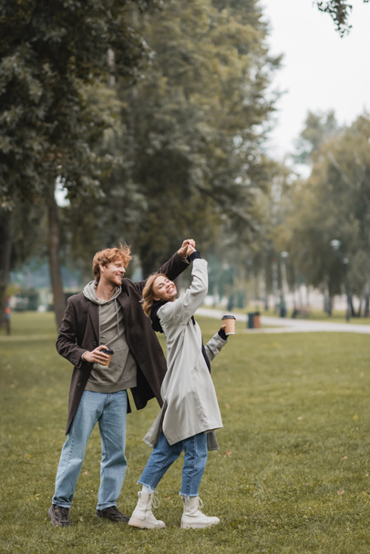 Uzun boylu mutlu kızıl adam ve neşeli kadın parkta dans ederken kahve tutuyor. - Fotoğraf, Görsel