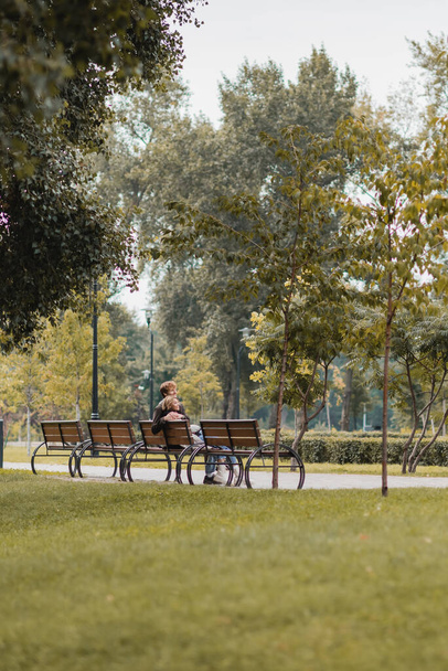 happy young man and woman hugging and sitting on wooden bench in green park - Valokuva, kuva