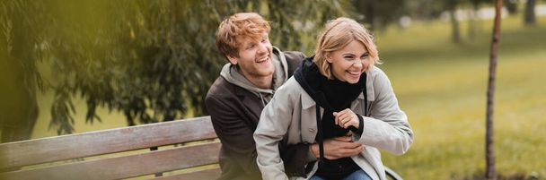 rousse homme souriant tout en chatouillant petite amie positive près du banc dans le parc, bannière - Photo, image