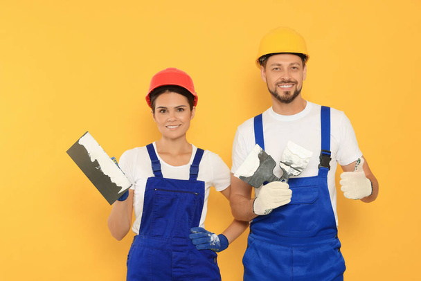 Professional workers with putty knives in hard hats on orange background - Fotografie, Obrázek