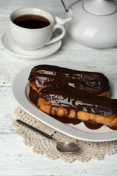 Tasty eclairs and cup of tea on wooden table - Фото, изображение