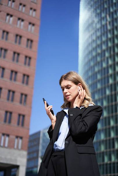 Portret van een succesvolle zakenvrouw met een telefoongesprek in een draadloze koptelefoon, lopend op straat. Bedrijfsvrouw met smartphone in het centrum. - Foto, afbeelding