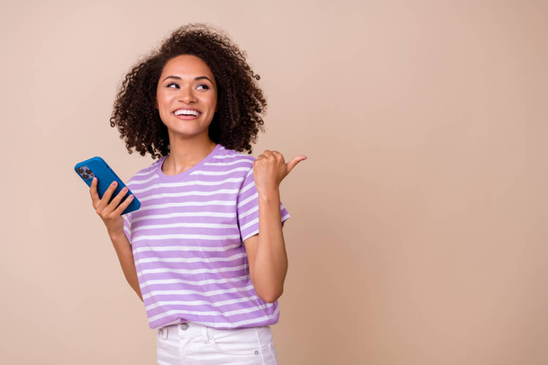 Φωτογραφία από χαριτωμένο αστείο κυρία φορούν βιολετί t-shirt κρατώντας σύγχρονη συσκευή δείχνοντας τον αντίχειρα κενό χώρο απομονωμένο μπεζ χρώμα φόντο. - Φωτογραφία, εικόνα