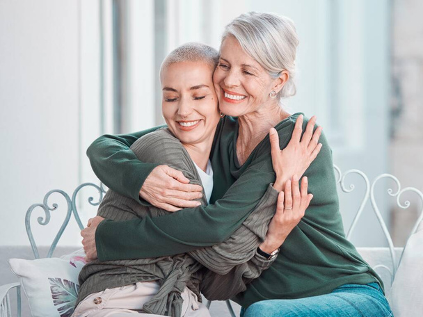 Cheerful senior mother hugging grownup daughter. Loving caucasian mom hugging her daughter while sitting together at home. Senior woman looking happy to see daughter during visit. - Foto, imagen