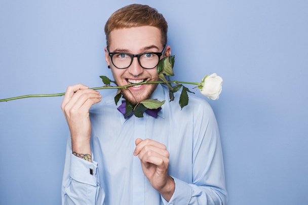Attractive young man smiling with a white rose in his mouth. Date, birthday, Valentine - Photo, image