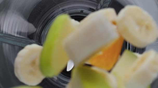 Close-up toevoegen van verse biologische vruchten stukken in elektrische blender bovenaanzicht. Lekkere banaan appel mandarijn vallende mixer kom in super slow motion. Natuurlijke ingrediënten voor gezonde vitamine cocktail. - Video