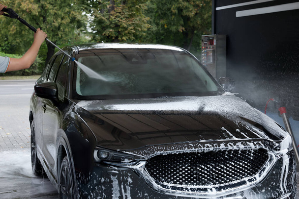 Man washing auto with high pressure water jet at car wash, closeup - Foto, afbeelding