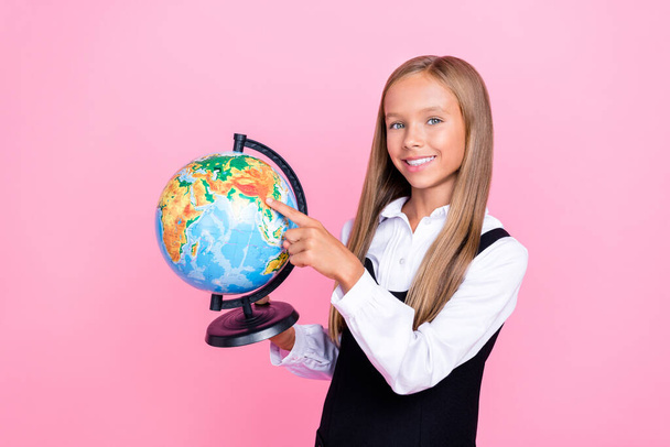 Portrait photo of little preteen child schoolgirl wear uniform blonde hair hold globe finger point map geography lesson isolated on pink color background. - Fotografie, Obrázek