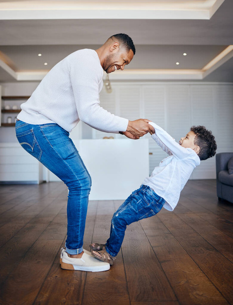 Little boy standing on dads feet and sharing a dance. Playful dad and son having fun together at home. Cheerful man teaching his son to dance. - Photo, Image