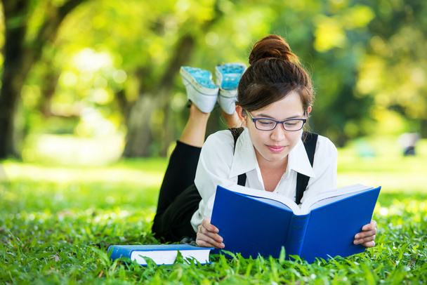 Lächelnder lässiger Student, der auf Gras liegt und Buch liest - Foto, Bild