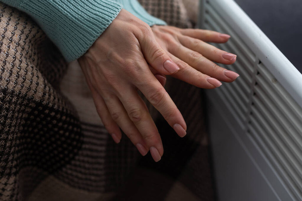Γυναίκα ζεσταίνει τα χέρια κοντά θερμάστρα σε εσωτερικούς χώρους, closeup. - Φωτογραφία, εικόνα