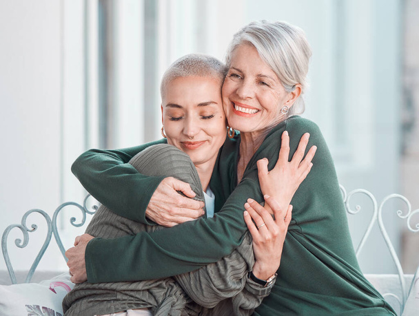 Cheerful senior mother hugging her adult daughter. Loving caucasian mom giving her daughter a hug while sitting on a chair together at home. Content woman bonding with her mother during a visit. - Foto, imagen