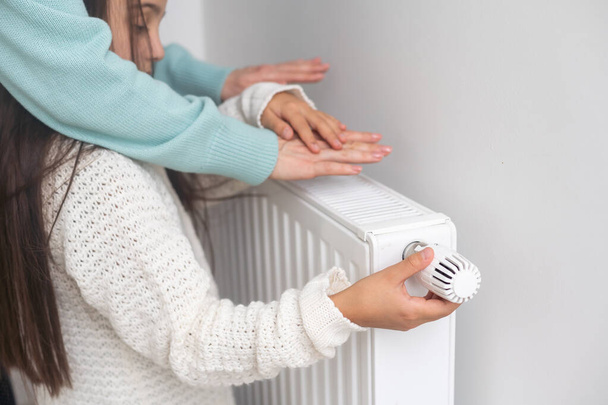 Girl warm ones hands near radiator at home - Foto, imagen