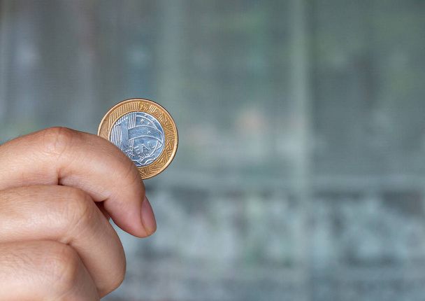 Одна настоящая монета на ладони у человека. Рука держит монету в 1 доллар. Реальная валютная система бразильского правительства - Фото, изображение