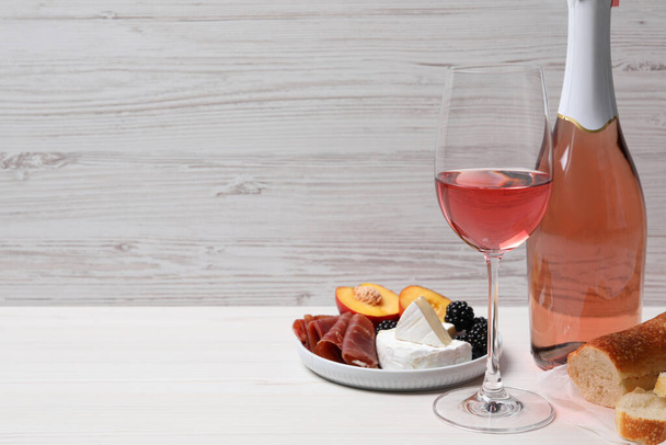 Delicious rose wine and snacks on white wooden table, space for text - Foto, Imagem