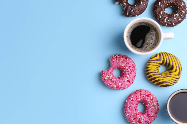 Deliciosas rosquillas y tazas de café sobre fondo azul claro, planas. Espacio para texto - Foto, imagen