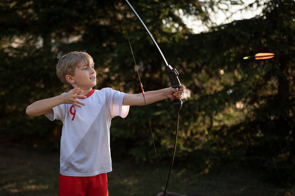 Мальчик стреляет из лука на открытом воздухе - Фото, изображение