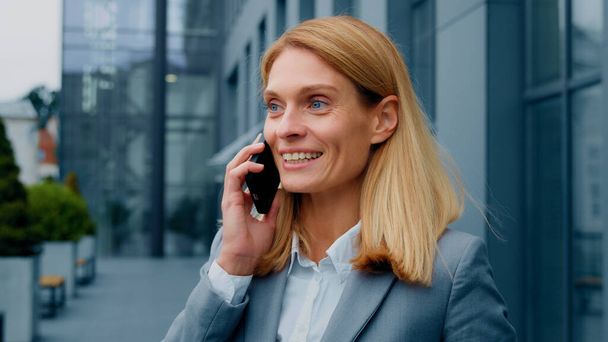 Happy enthusiastic excited woman talking on mobile phone outdoors sharing good experience with friend remotely chatting on smartphone joyful businesswoman speaks on telephone communicating with client - Photo, Image