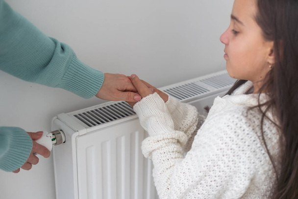 Meisje warm degenen handen in de buurt radiator thuis - Foto, afbeelding