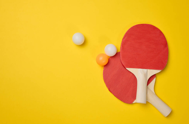 Dvojice dřevěných tenisových raket pro ping pong a plastové míčky na žlutém pozadí, horní pohled - Fotografie, Obrázek