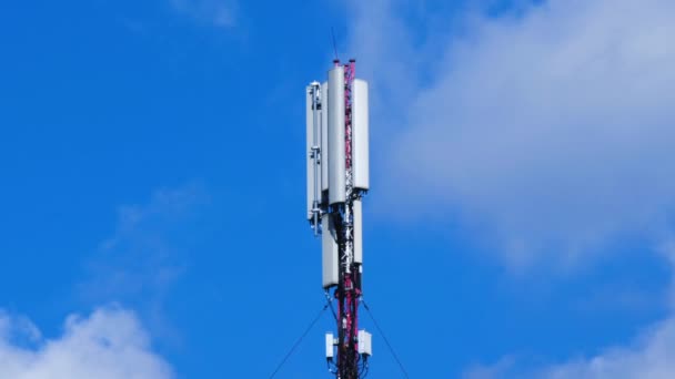 Antena komórkowa na tle niebieskiego nieba i białych chmur. Stacja bazowa wieży komórkowej ze sprzętem łączności elektronicznej. Wieża komórkowa ze sprzętem telekomunikacyjnym. Miejsce na tekst - Materiał filmowy, wideo