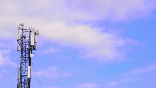 Antena del sitio de la célula sobre nubes blancas y fondo azul del cielo. Torre celular con equipo móvil de telecomunicaciones. Estación base torre celular con equipo de comunicaciones electrónicas. Lugar para el texto - Metraje, vídeo
