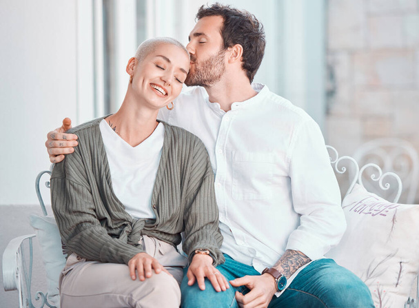 Affectionate young caucasian couple embracing while relaxing together at home. Happy boyfriend hugging and kissing girlfriend on the head while sharing an intimate moment in a loving relationship. - Photo, Image