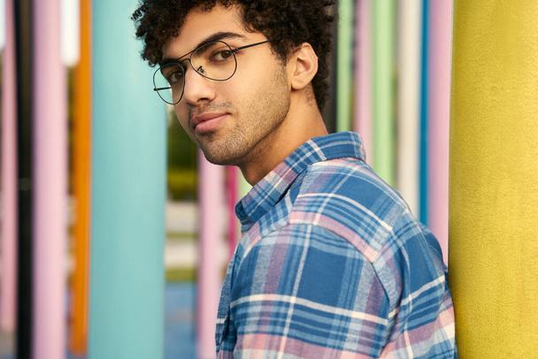 Portrait of handsome stylish middle eastern man wearing glasses looking at camera  standing near colorful background. Young fashion model posing for pictures - Foto, afbeelding