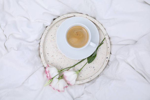 Tray with cup of coffee and flowers on white bed, top view - Foto, imagen