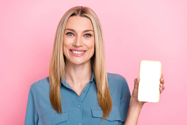 Retrato de mulher radiante de dentes alegre com cabelo loiro demonstrando touchscreen promovendo aplicativo isolado no fundo cor-de-rosa. - Foto, Imagem