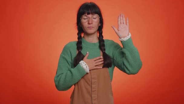I swear to be honest. Sincere responsible young nerd woman raising hand to take oath, promising to be honest and to tell truth, keeping hand on chest. Latin girl isolated on studio orange background - Footage, Video