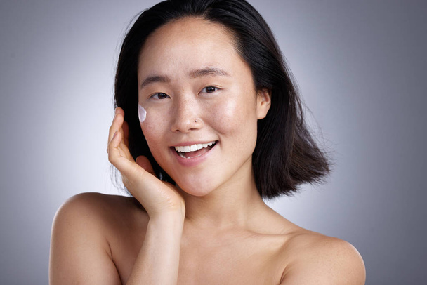 ¿Estás cuidando tu piel? una mujer joven aplicando loción sobre un fondo gris - Foto, Imagen