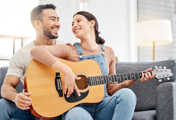 Verbinding maken met muziek. een jong stel spelen gitaar terwijl samen ontspannen op een bank thuis - Foto, afbeelding