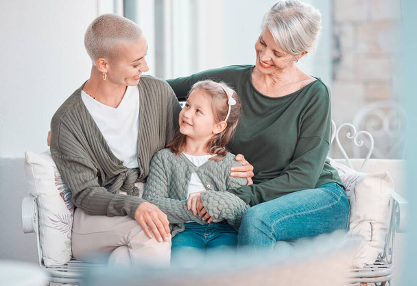 Три поколения женщин сидят вместе и смотрят друг на друга. Очаровательная маленькая девочка сближается со своей матерью и бабушкой дома. - Фото, изображение